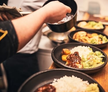 Professional chef plating gourmet chicken and rice bowls with salad in a commercial kitchen.