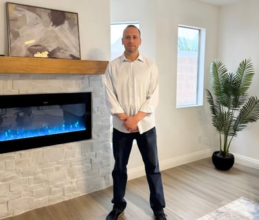Professional man standing in a modern living room next to a white stone fireplace with blue flames.