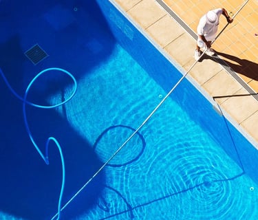 Technician using a vacuum pole to clean a backyard pool—illustrating weekly pool maintenance service in action.