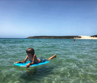 Vista del cabo y duna de Bolonia desde el aguay un niño en un board. Tarifa, provincia de Cádiz