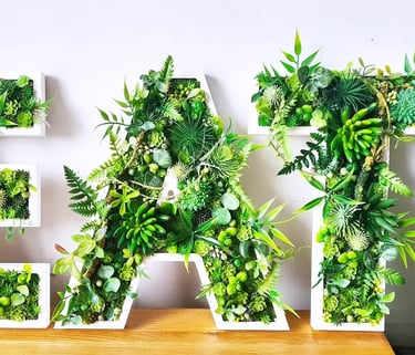 Decorative wall art spelling EAT using artificial succulents, moss, and green plants in white letter frames.