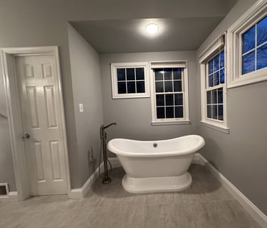 close-up of freestanding bathtub with stainless steel floor-mounted tub filler and windows