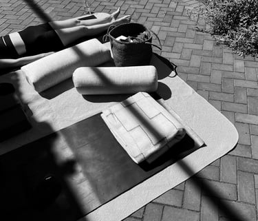 Black and white image of an outdoor Personalized Yoga session with a client in savasana, surrounded by bolsters and props