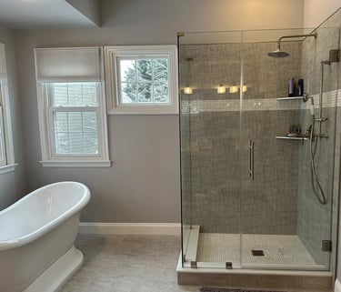 Renovated bathroom with white freestanding bathtub, stainless steel tub filler, and glass shower