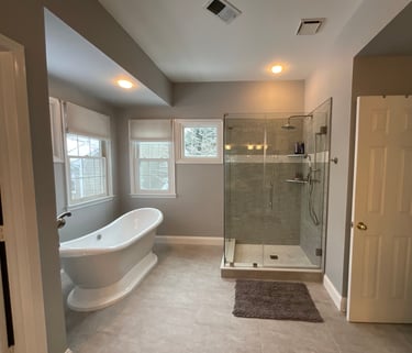 Renovated bathroom with white freestanding bathtub, stainless steel tub filler, and glass shower
