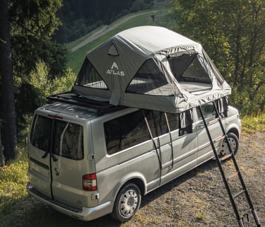 Atlas roof top tent mounted on a silver Volkswagen camper van parked in a scenic mountain forest.
