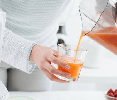 a person pouring a drink into a glass of juice