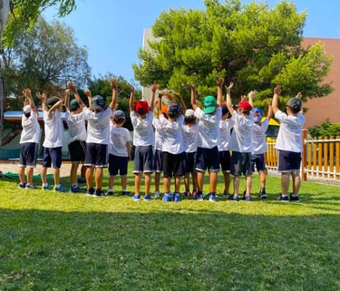 Παιδιά με καλοκαιρινές στολές και καπέλα υψώνουν τα χέρια τους στον αέρα, συμμετέχοντας σε δραστηριό