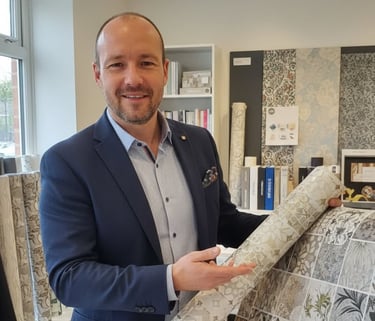 Professional interior designer presenting a roll of floral and geometric patterned wallpaper in a showroom.