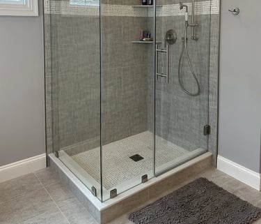 Modern walk-in shower with glass panels, stainless steel fixtures, and mosaic tile floor