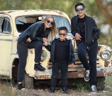 mamá, hijo pequeño e hijo mayor posados cerca de un coche antiguo en el bosque