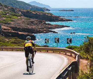 Cyclist on the scenic Alghero-Bosa road in Sardinia with Mediterranean sea view.