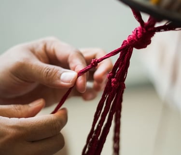 Primer plano de manos realizando nudos con hilo rojo para una pieza artesanal.