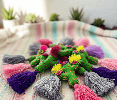 Handmade green felt cactus ornaments with colorful tassels and embroidery on a striped fabric.