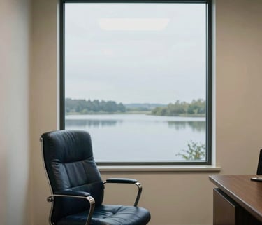 A serene North American office interior with a large window overlooking a calm landscape, ivory walls, and a navy leather chair.