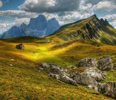 Panoramic view of the green slopes and jagged peaks in the Italian Dolomites under a cloudy sky.