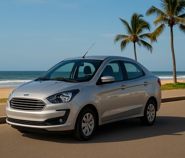 Ford Ka Sedan prateado estacionado próximo à praia com mar e coqueiros ao fundo em dia ensolarado.
