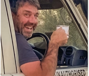Herve Fritz laughing whilst driving with coffee in hand