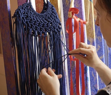 Tapete de macramé hecho a mano en azul marino, siendo tejido por un artista en un telar vertical
