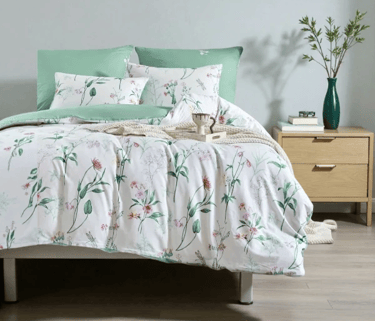 Modern bedroom featuring a white floral duvet set with sage green pillows on a wooden bed frame.