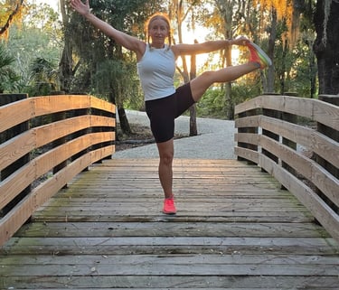Eva practicing balance yoga pose on a wooden bridge at sunset, surrounded by nature.