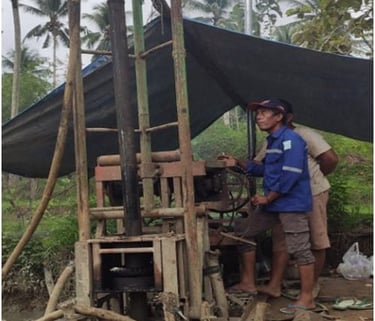 A worker operates a portable water well drilling rig at an outdoor construction site.