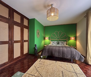 Tropical style bedroom with green walls, rattan headboard, bamboo light, and woven wardrobe doors.