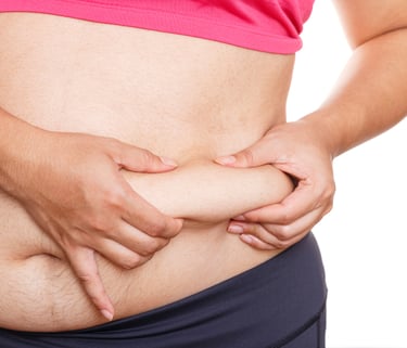 A woman pinching excess belly fat on her stomach to show weight gain or weight loss progress.