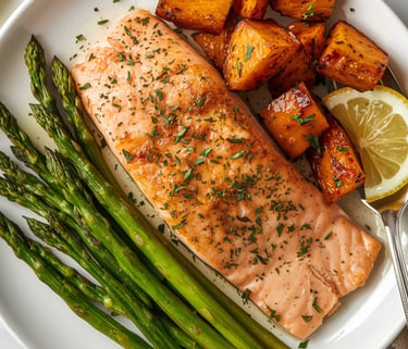 Pan-seared salmon fillet served with roasted sweet potatoes, green asparagus, and a lemon wedge.