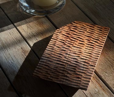 Hand-carved rustic wooden vase displayed on a natural wood slice pedestal under warm sunlight.
