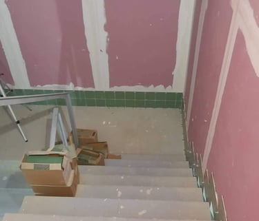 Concrete stairs under renovation with pink drywall and green ceramic tile backsplash installation.