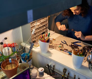 Joyera utilizando alicates en su estación de trabajo artesanal con cuentas de vidrio y materiales