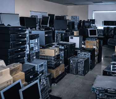 A room filled with stacks of recycled Dell computers, Cisco hardware, and old monitors for electronic waste disposal.