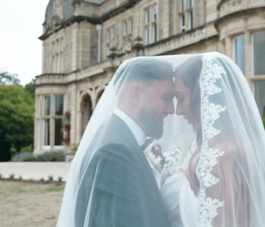 Bride and groom pose together in front of a large, elegant building, celebrating their wedding day.