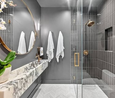 Bathroom remodel with a wall-mounted sink, round mirror, and glass-enclosed shower.