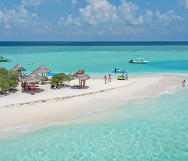 Aerial view of a tropical sandbar with turquoise water, palm umbrellas, and tourists in the Maldives.