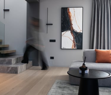 Modern living room interior with grey sofa, abstract wall art, and floating wooden stairs.