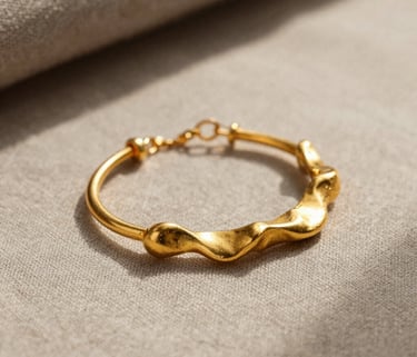 A professional close-up photograph of handcrafted gold jewelry featuring organic shapes, resting on a soft taupe linen surface in a North American studio with warm, diffused sunlight.