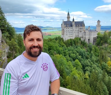Smiling man in a white soccer jersey at Neuschwanstein Castle viewpoint in Germany.