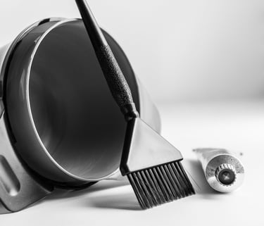 a black hair coloring bowl with brush leaning against it, hair color tube beside it