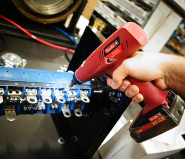 A technician uses a Desoutter cordless electric nutrunner to assemble an industrial electrical component.
