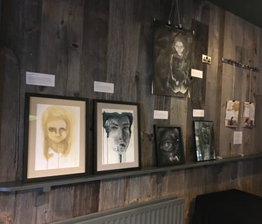 wood panelled wall with art works on the wall and shelf. Dark colours. White labels.