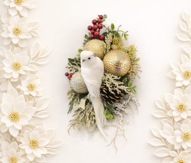 Elegant white bird ornament nestled in a gold Christmas wreath with paper flowers and holly berries.