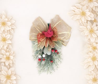 Festive Christmas swag decoration with a red bird, gold ribbon bow, and berries framed by white flowers.