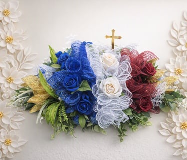 Patriotic floral arrangement with red, white, and blue roses, mesh ribbon, and a gold cross.
