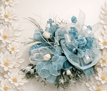 Blue and white artificial flower arrangement with deco mesh ribbons and a small blue cross.