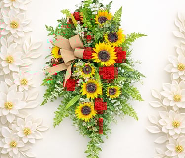 Sunflower and red carnation floral swag with burlap bow and green ferns for home wall decor.