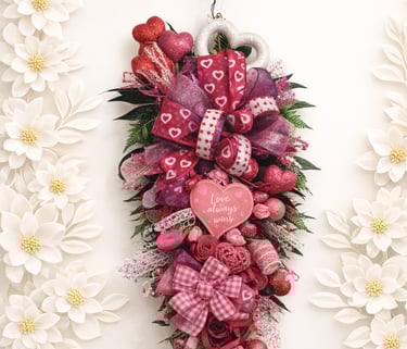 Valentine's Day door swag wreath featuring pink ribbons, glitter hearts, and Love Always Wins sign.