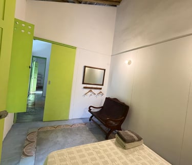 Rustic bedroom with lime green doors, bamboo ceiling, wooden bench, and white bed linens.
