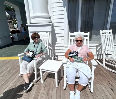 A picture of 2 women sitting in rocking chairs on the porch of the hotel.